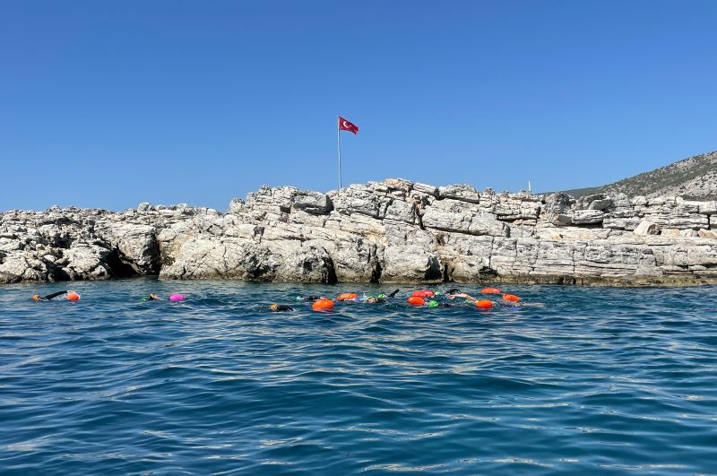 Gruppe mit orangen Schwimmbojen im Meer vor einer Felsinsel bei Bodrum